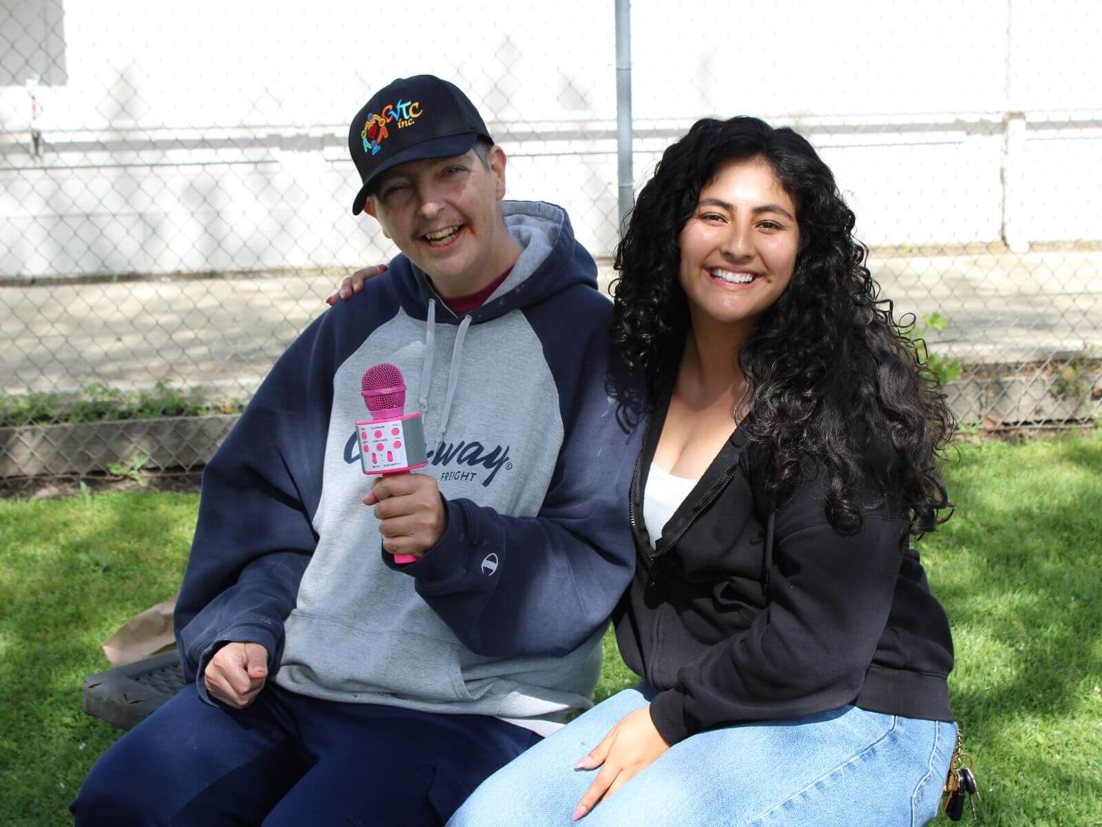 CV Training Center consumer smiling while holding a pink microphone  with staff during an outdoor community life skills program in Stockton, CA