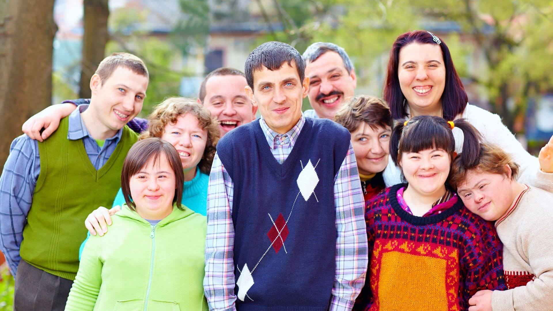Group of adults with developmental disabilities smiling together outdoors in community setting