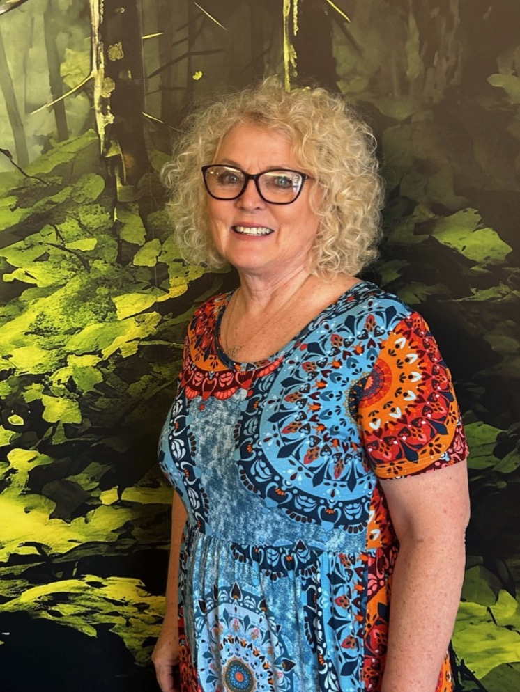 Judy J. standing in front of a painting of a forest.