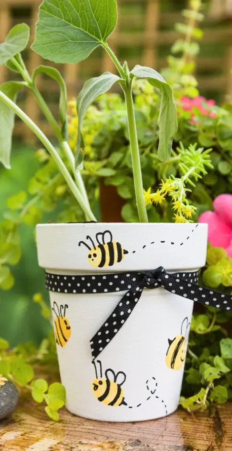 A hand-painted outdoor flower pot featuring cheerful bee designs, complete with a plant inside. 