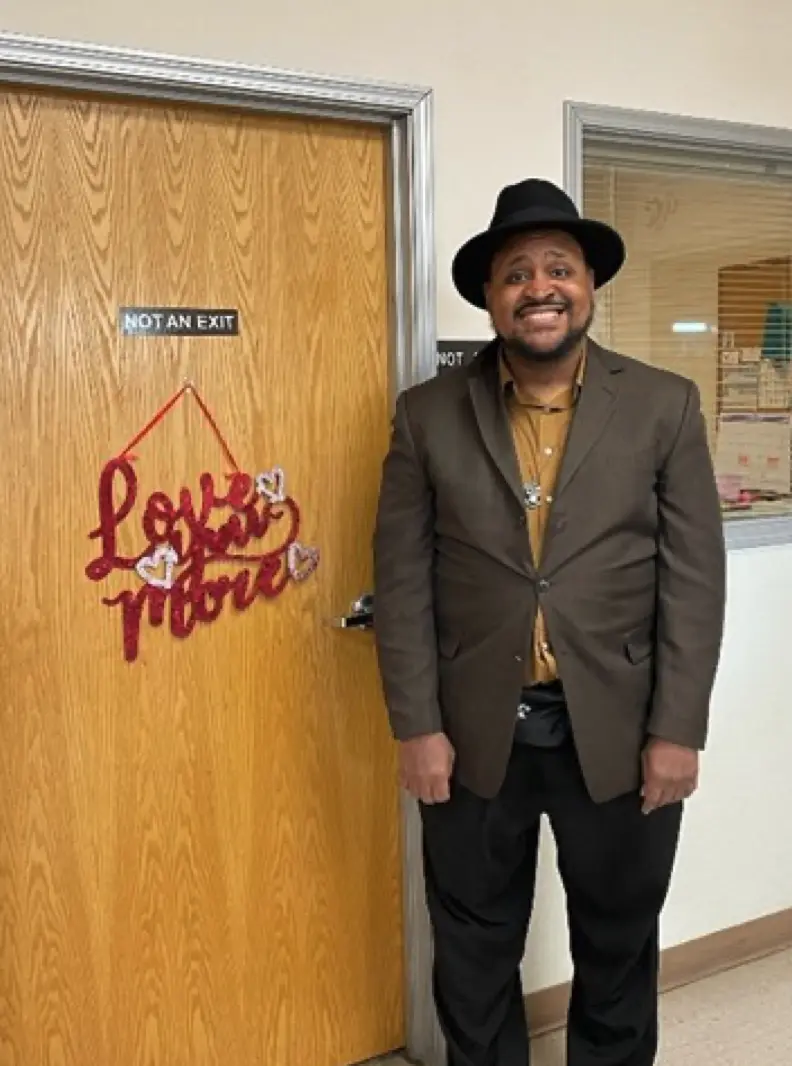 Michael standing in front of a door with a sign reading Love You More.