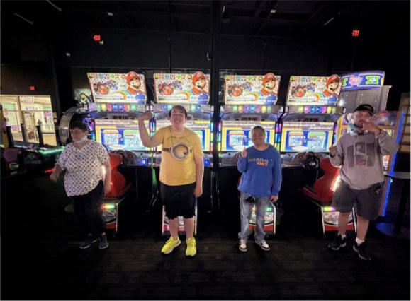 Four members of Team Dynasty standing in front of a row of Mario Kart arcade machines.